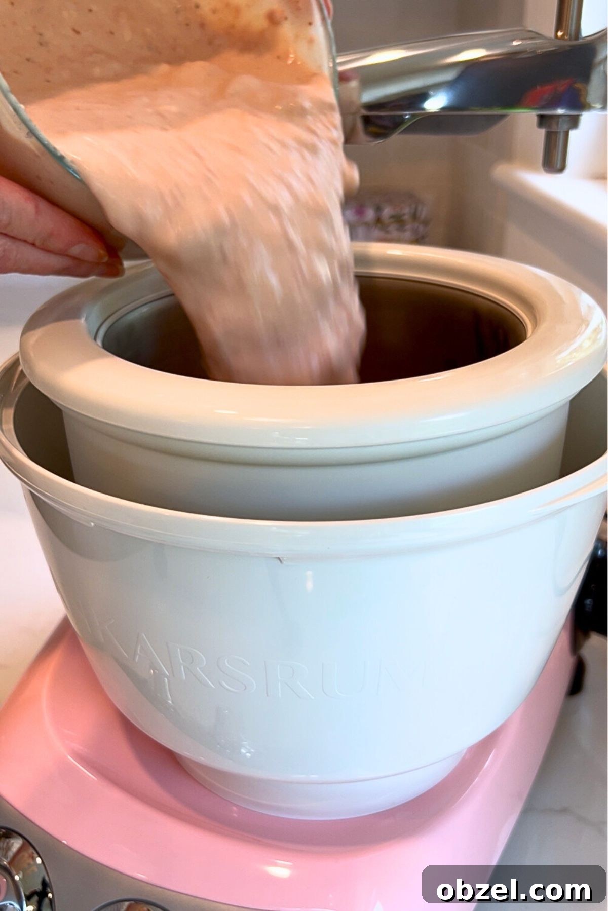 Pouring the strawberry ice cream base into the Cloudy Pink Ankarsrum Assistent Original Mixer and ice cream maker on low speed.