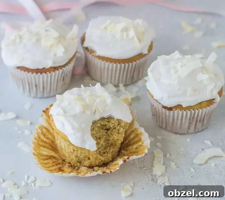Gluten-Free Coconut Cupcakes with Fluffy Frosting 6 cupcake with a bite taken out of it with more gluten-free coconut cupcakes in the background