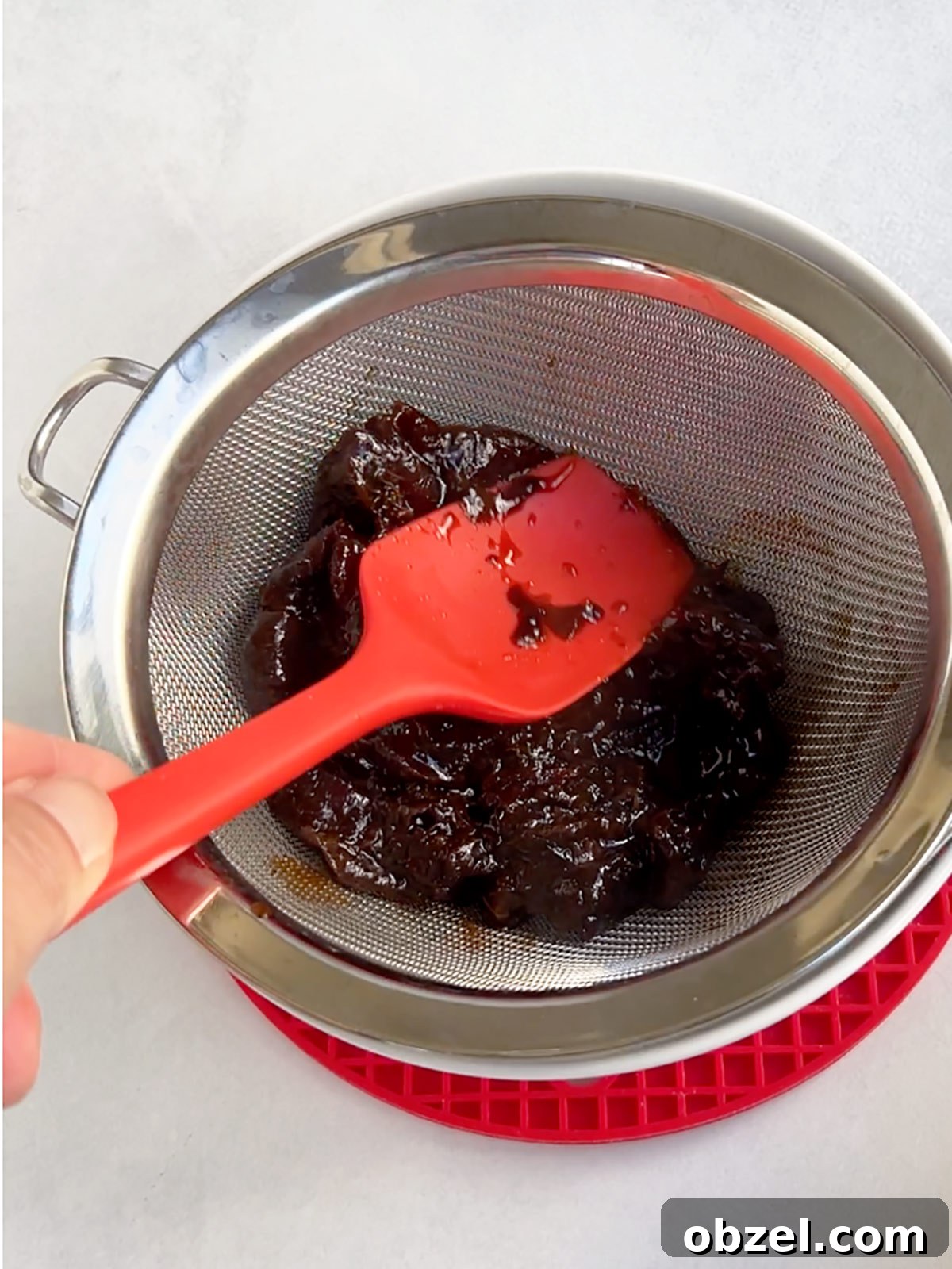 How to Make Lekvar Prune Butter at Home 7 Prune filling being strained with a red spatula.