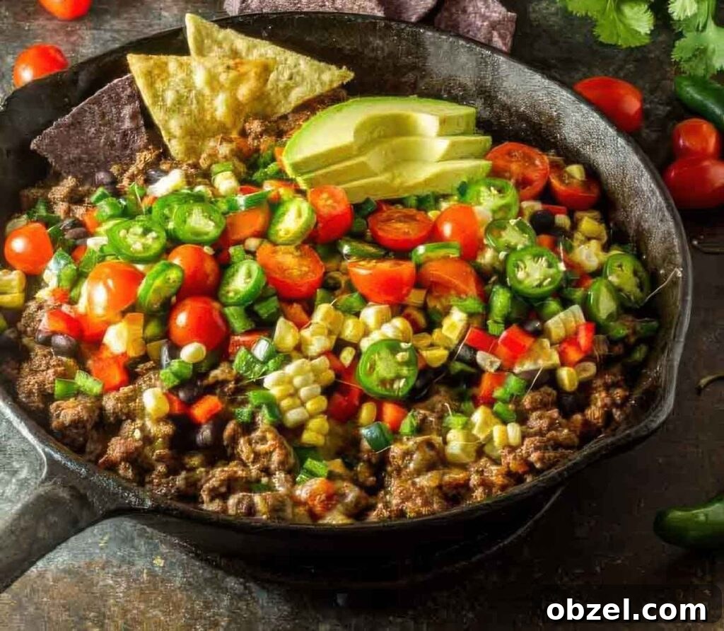 Top-down image of loaded healthy nachos with fresh jalapeños, corn, cherry tomatoes, red bell peppers, and black beans in a skillet, garnished with avocado and tortilla chips.