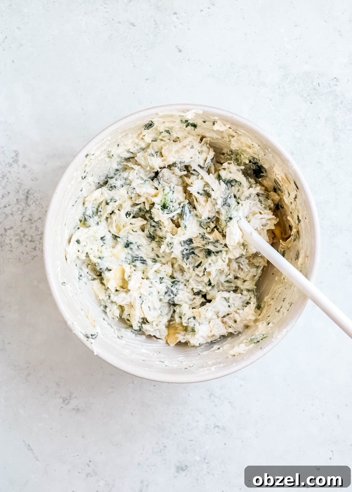 Creamy Spinach Artichoke Dip Recipe 7 mixed up cream cheese, mayonnaise, yogurt, spinach, artichokes, seasonings, and cheese in a white bowl
