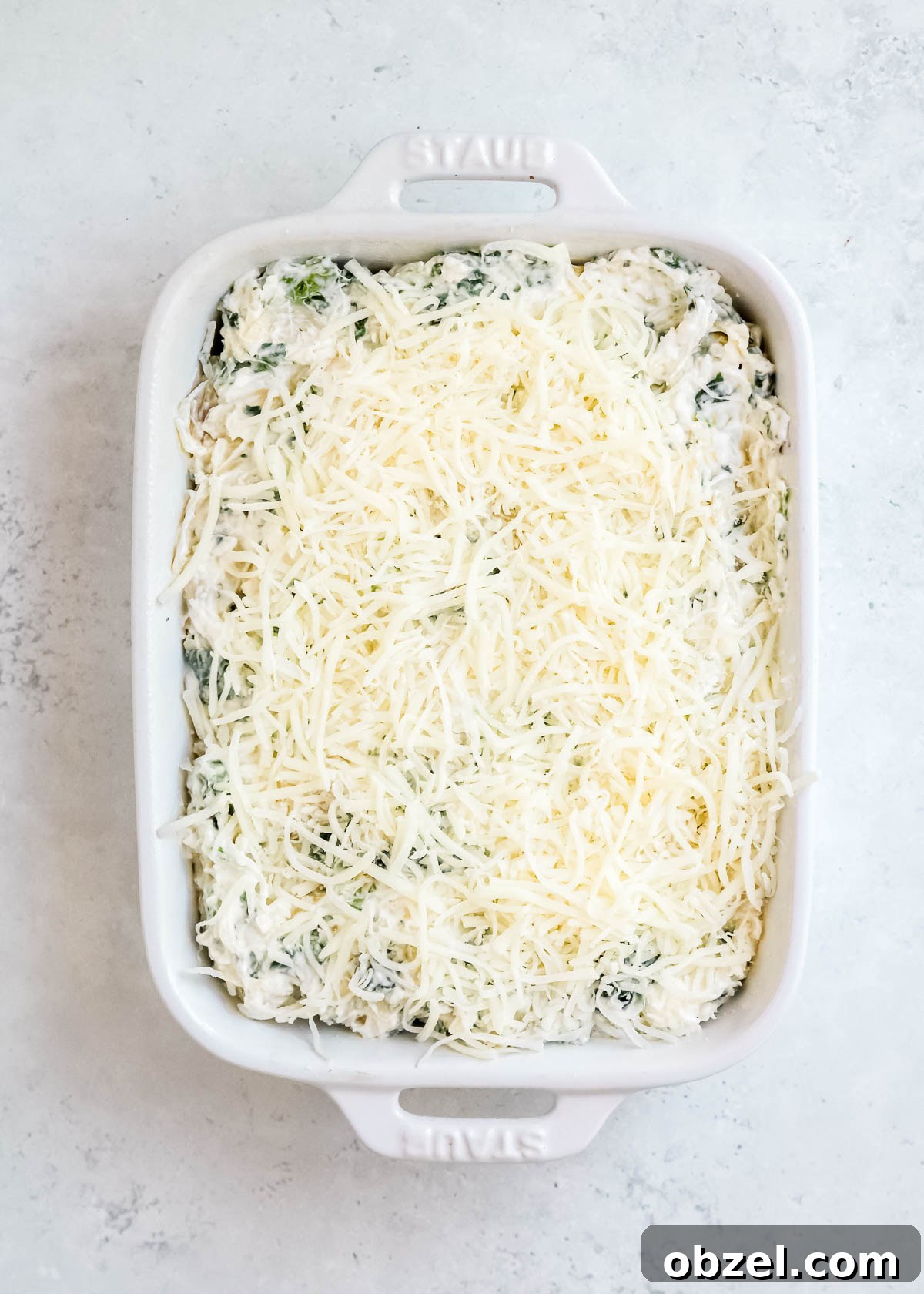 Creamy Spinach Artichoke Dip Recipe 9 spinach dip topped with shredded cheese in a white rectangular baking dish