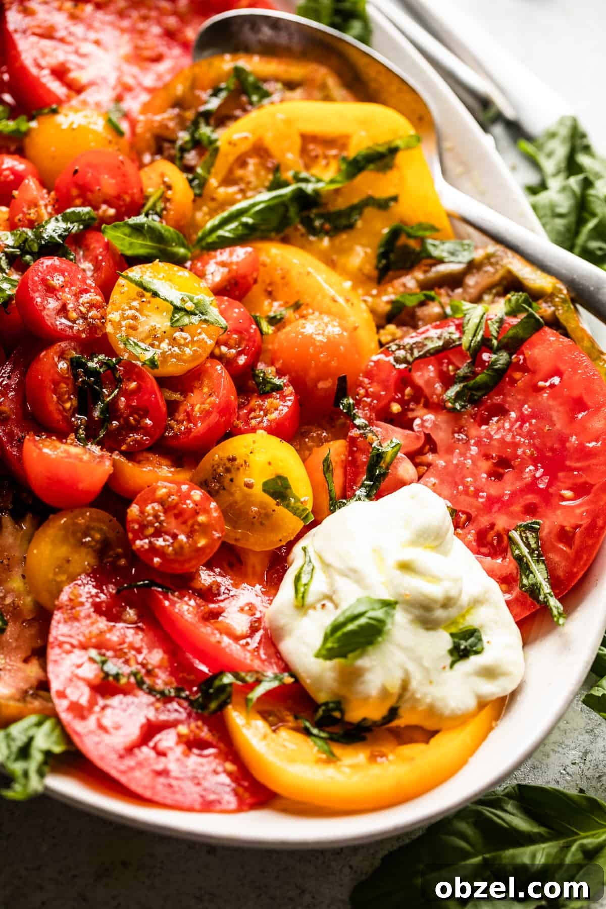 Tomato Burrata Salad: slices of heirloom tomatoes arranged on an oval platter with burrata and basil.