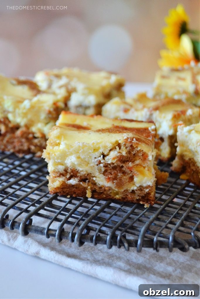 Carrot Cake Cheesecake Bars Recipe 4 an arrangement of carrot cake cheesecake bars on a black wire rack sits against a light spotted background. some yellow flowers are off to the right in the background.