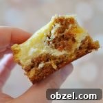 Carrot Cake Cheesecake Bars Recipe 5 the photographer is holding a carrot cake cheesecake bar against a lightly colored dotted background.