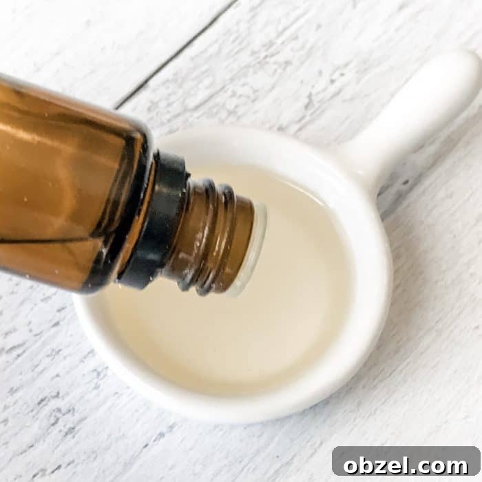 DIY Peppermint Candy Cane Lip Scrub for Soft Lips 8 adding peppermint essential oil dropped from bottle into apricot kernel oil in measuring spoon for use in peppermint candy cane lip scrub with essential oils