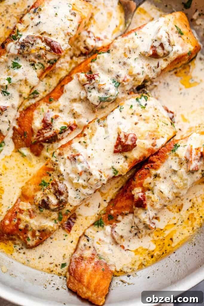 overhead shot of four salmon fillets in a skillet with cream sauce
