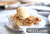 small white plate with a slice of dutch apple pie on it and a fork. there is also a scoop of ice cream on top of the pie