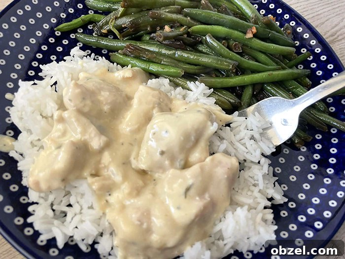 Creamy Italian chicken sauce served over white rice next to a serving of green beans on a dark blue plate with white polka dots with a fork sitting on the plate partially under the rice.