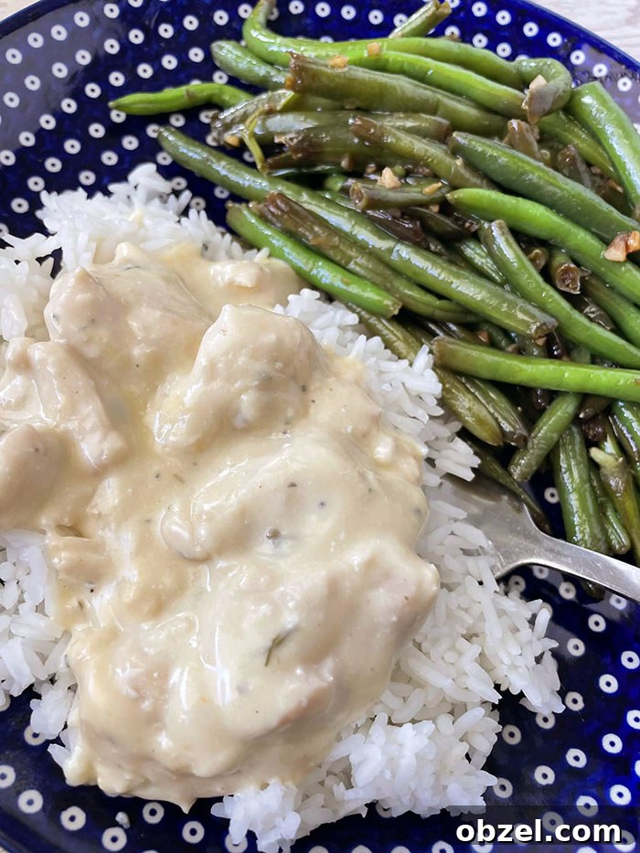 A dark blue Polish pottery dinner plate with white polka dots with a serving of green beans and creamy italian chicken served over white rice with a fork inserted partially under the rice on the plate.