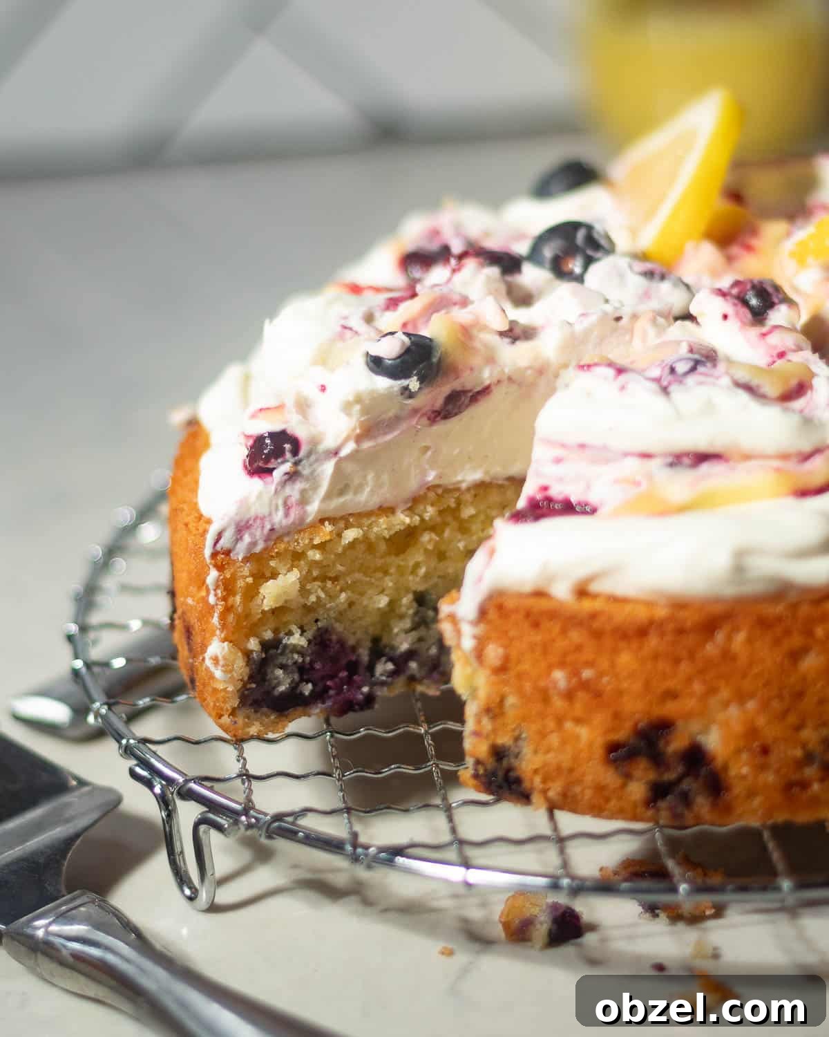 Lemon Blueberry Cake with Mascarpone Frosting 3 Side view of a sliced lemon blueberry mascarpone cake on a wire rack, showing blueberries and mascarpone topping.