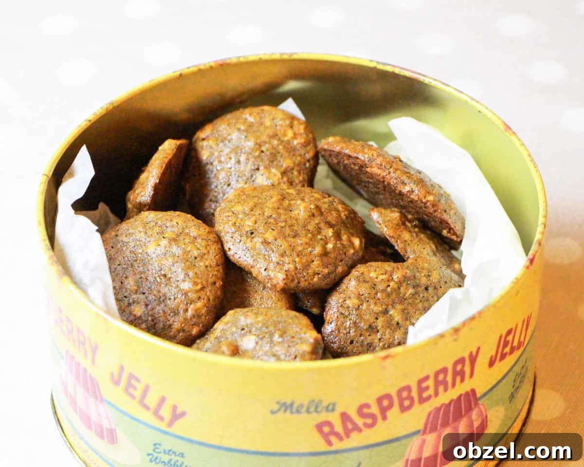 An old-fashioned cake tin filled with zesty orange and walnut cookies on a spotty taupe and white tablecloth.