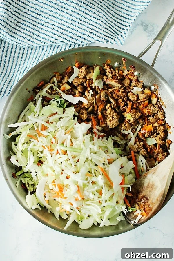 How to make Egg Roll in a Bowl, a low-carb dinner just like takeout. Overhead shot of cooked ground meat with coleslaw mix in skillet.