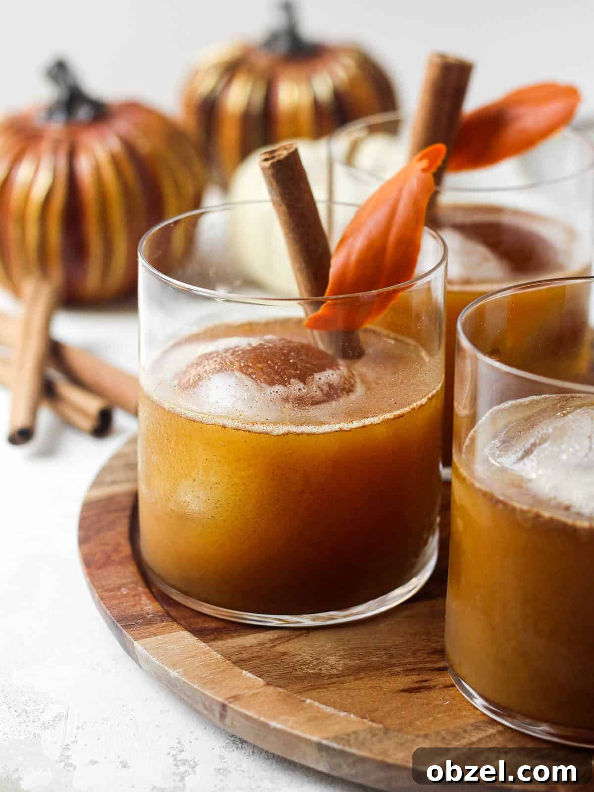 Fall bourbon cocktail on wooden tray with ice ball and cinnamon stick.