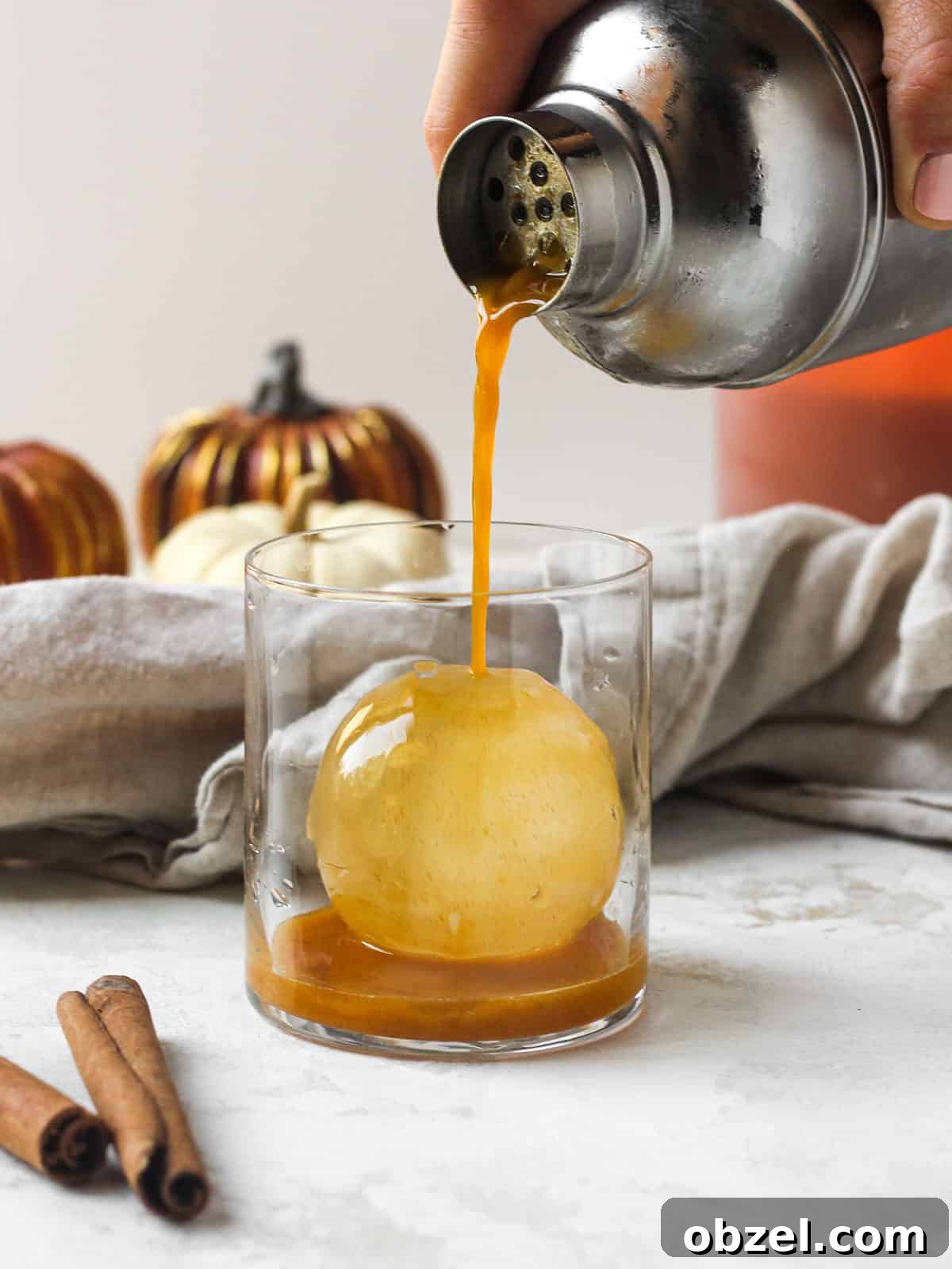 Bourbon Fall cocktail being poured into whiskey glass on ice ball.