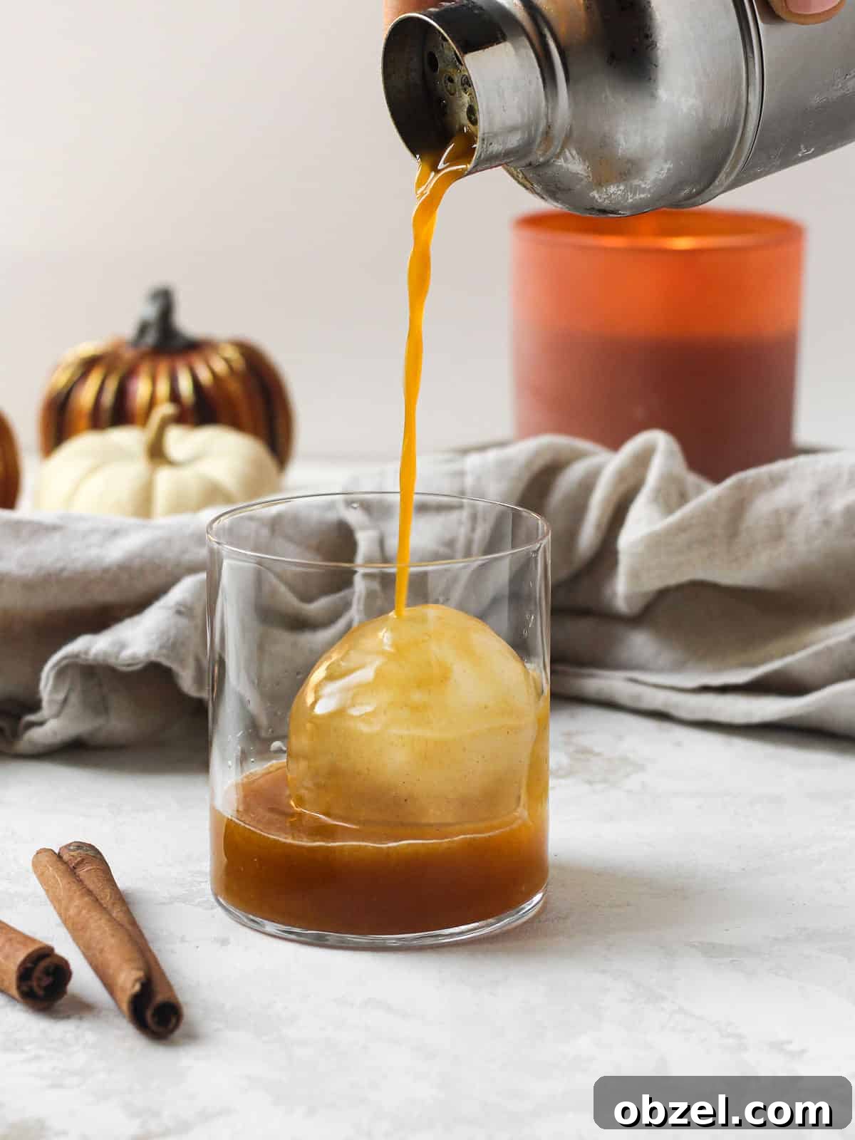 Bourbon Fall cocktail being poured into whiskey glass on ice ball.