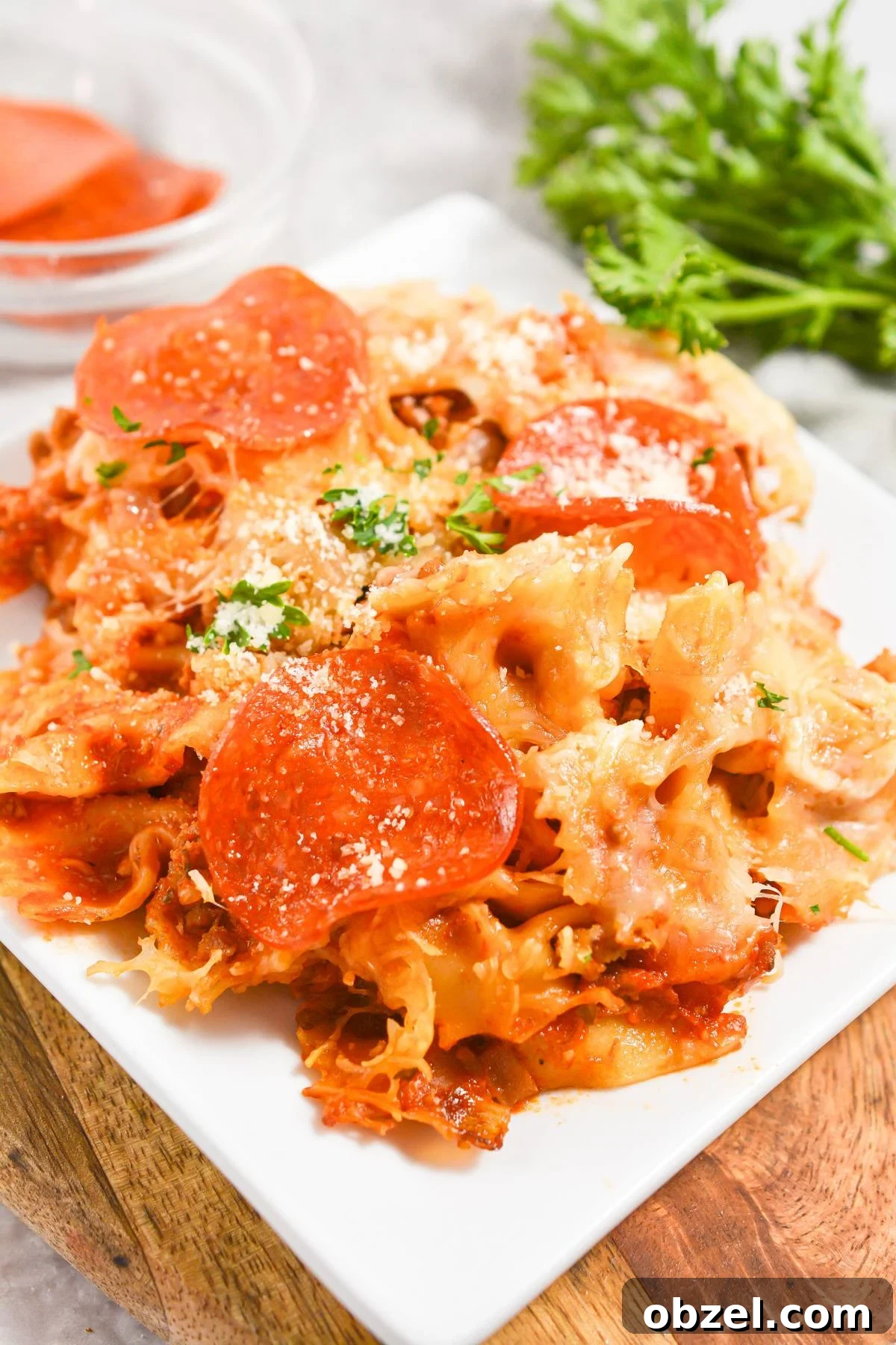Crock Pot Pizza Casserole with Pasta and Pepperoni 2 A white plate with a portion of pizza pasta casserole, garnished with parsley.