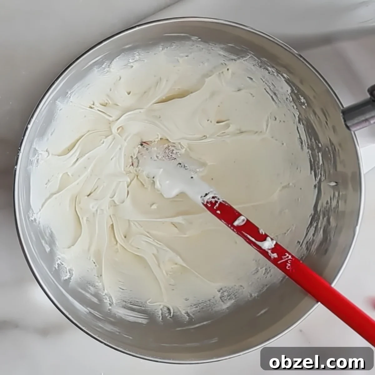 white frosting inside steel bowl with red little spatula on top.