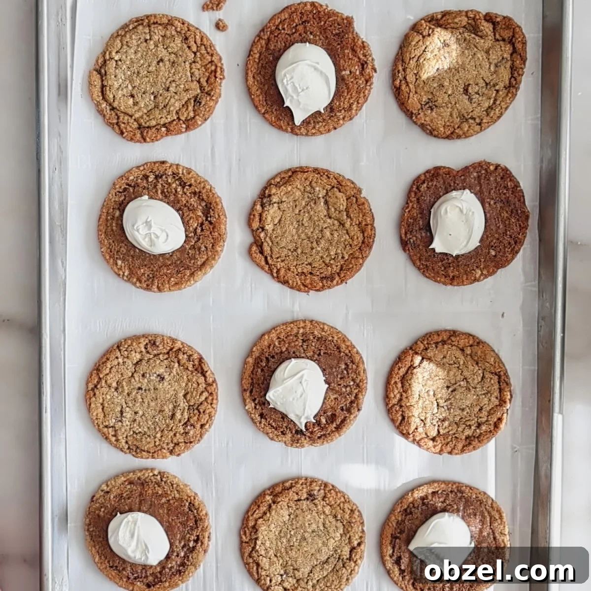 white frosting scooped on every other upside down cookie on parchment-lined baking sheet.