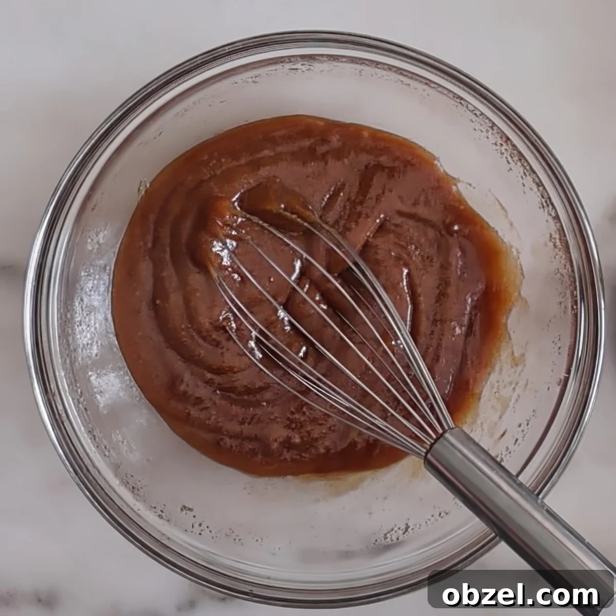 dark brown ingredients in glass bowl with wire whisk.
