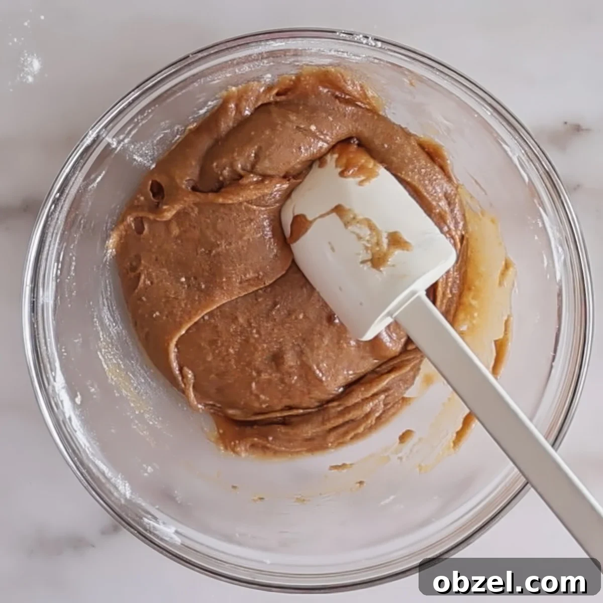 light brown mixture in glass bowl with white silicone spatula.
