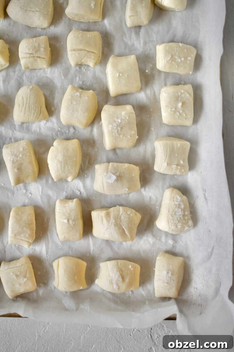Dipped dough lined up on a sheet pan and some of the pretzel bites dusted with flakey salt, before baking.