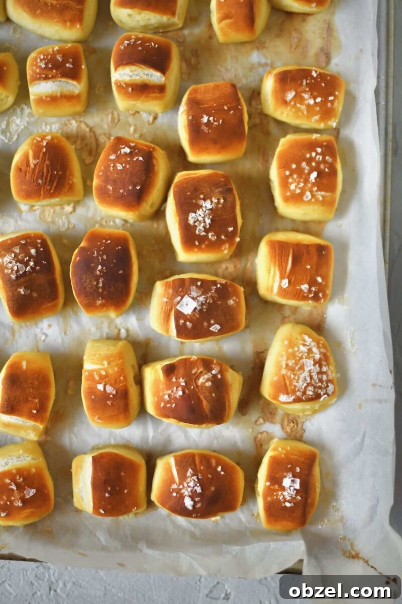 Pretzel bites lined up on a sheet pan and some of the dusted with flakey salt, after baking.