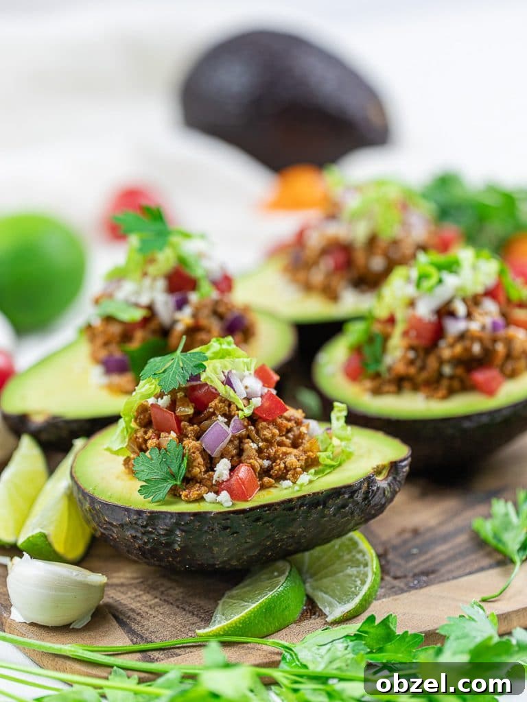 Keto Taco Stuffed Avocado boats on a wooden cutting board with lime, taco meat, tomatoes, and cilantro