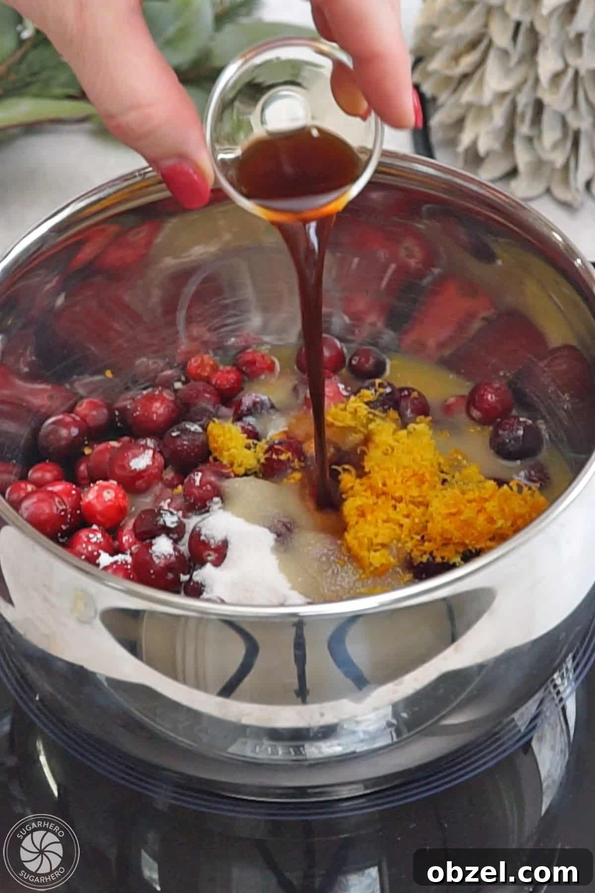 Cranberry Orange Sauce Recipe 9 Hand pouring vanilla into a pot filled with the other ingredients for cranberry sauce.