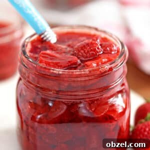 Glass jar of Strawberry Sauce with blue spoon sticking out.