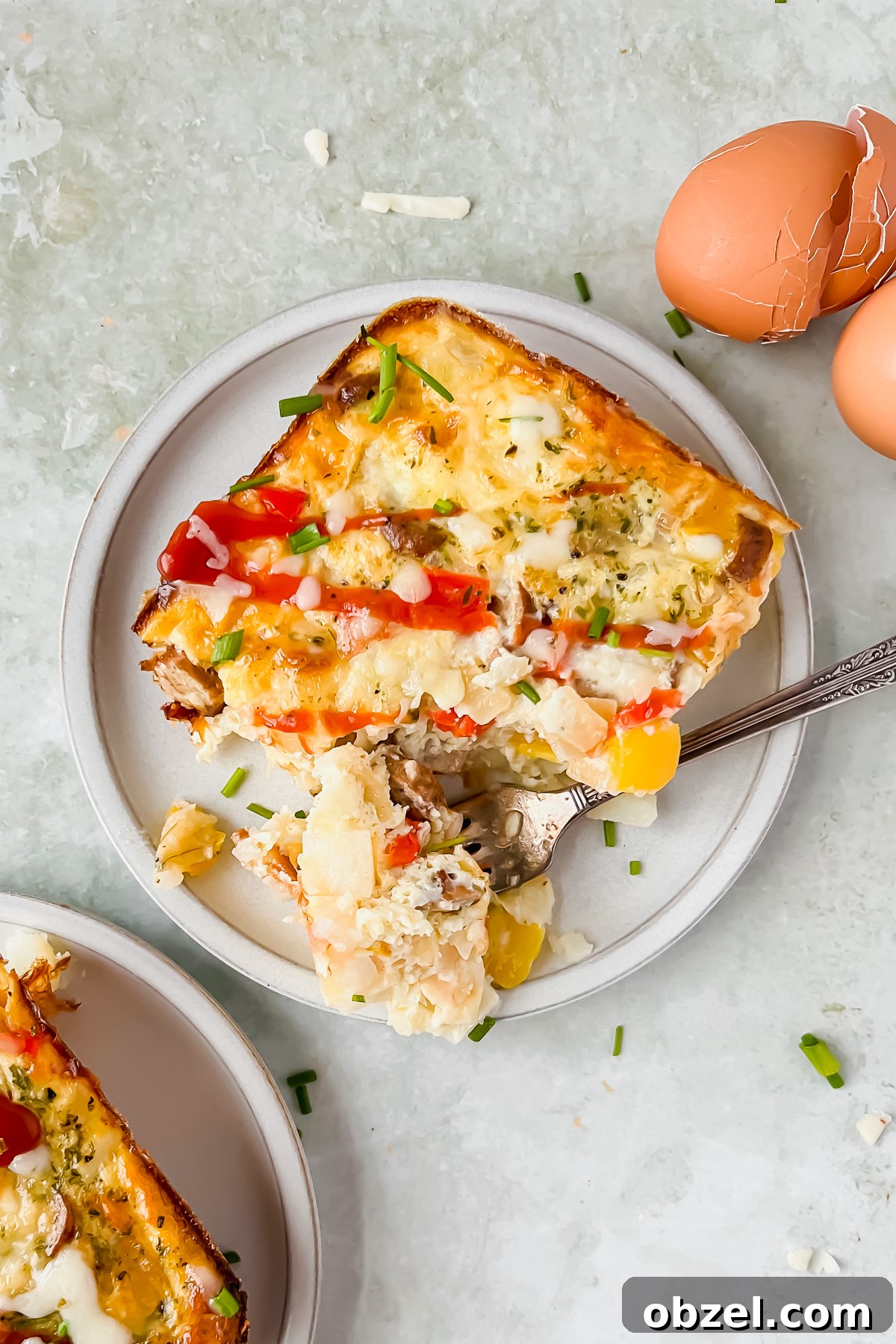 Cheesy Loaded Hashbrown Casserole with Bacon 2 slice of loaded hashbrown casserole on white serving plate beside egg shells.