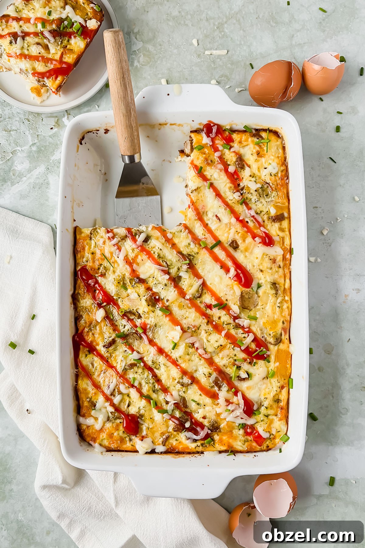 Cheesy Loaded Hashbrown Casserole with Bacon 6 baked loaded hashbrown casserole in white baking dish drizzled with ketchup with slice taken out and put on plate