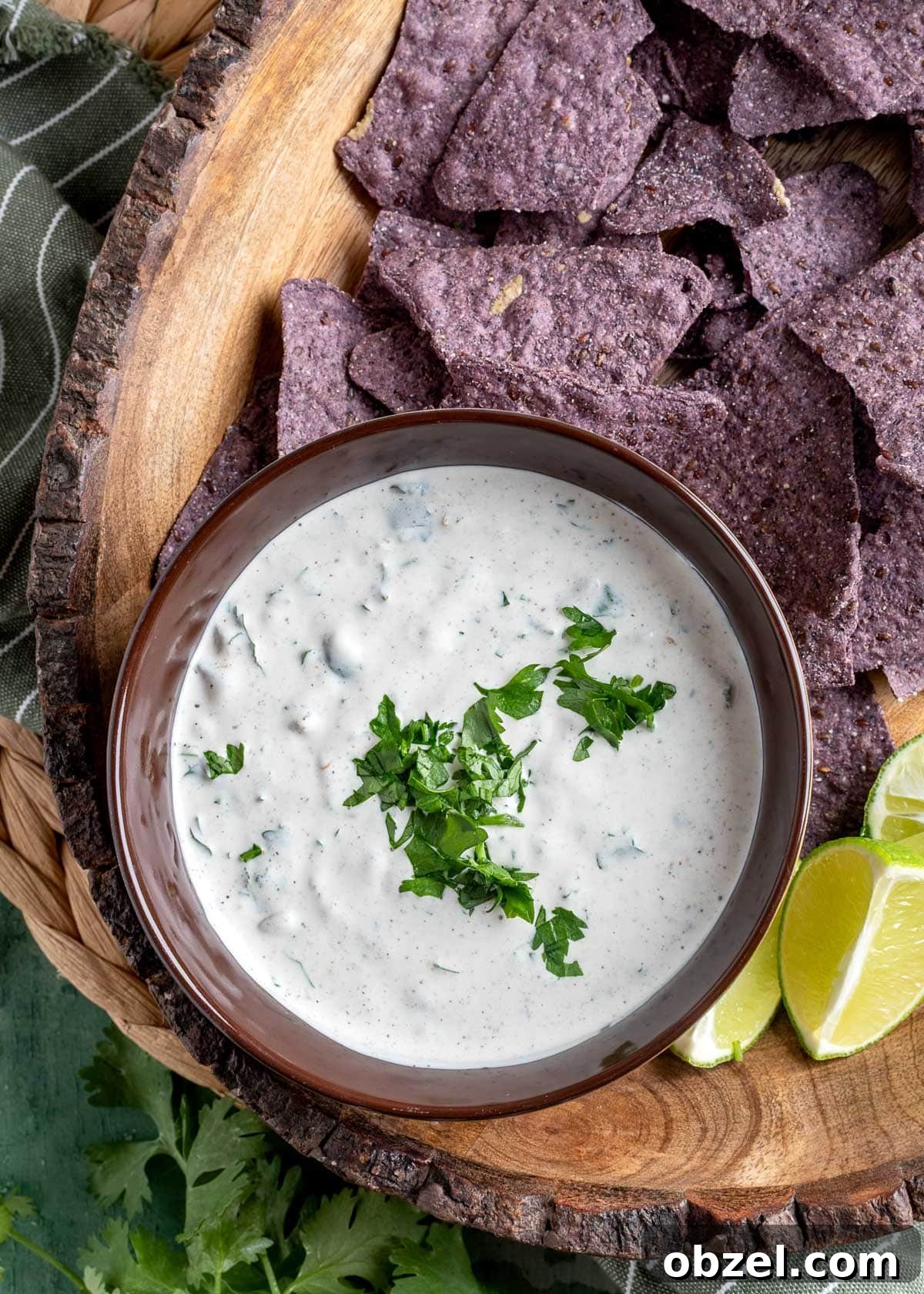 Creamy Green Chile Cilantro Dip 2 overhead of green chile dip with cilantro in a brown bowl on a platter with blue corn tortilla chips and lime wedges