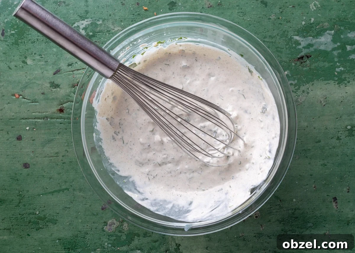 Creamy Green Chile Cilantro Dip 5 green chile cilantro dip mixed in a glass bowl with a stainless steel whisk on a green board