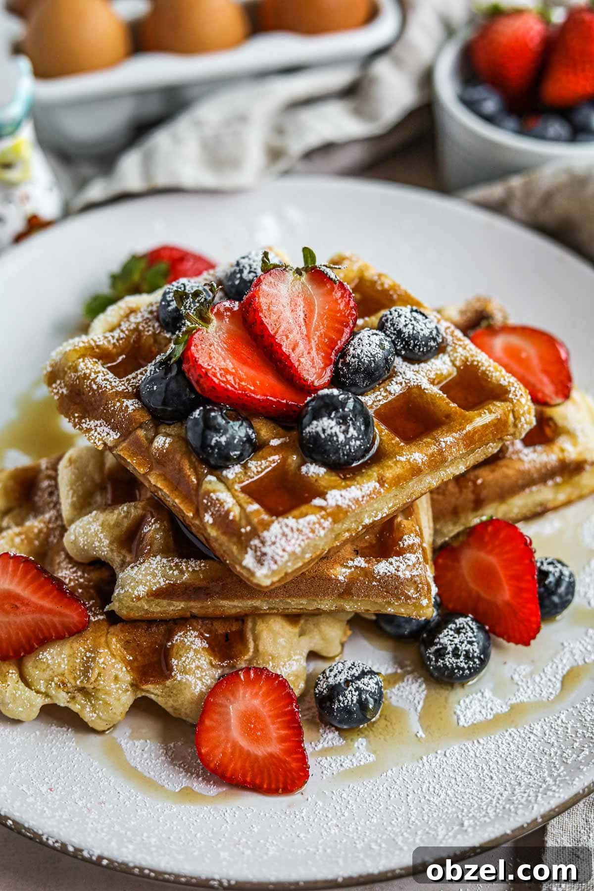 Gluten Free Mochi Waffles with Crispy Chewy Texture 2 Gluten-free mochi waffles stacked on a plate with berries, maple syrup, and powdered sugar.