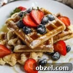 Gluten Free Mochi Waffles with Crispy Chewy Texture 7 Gluten-free mochi waffles stacked on a plate with berries, maple syrup, and powdered sugar.
