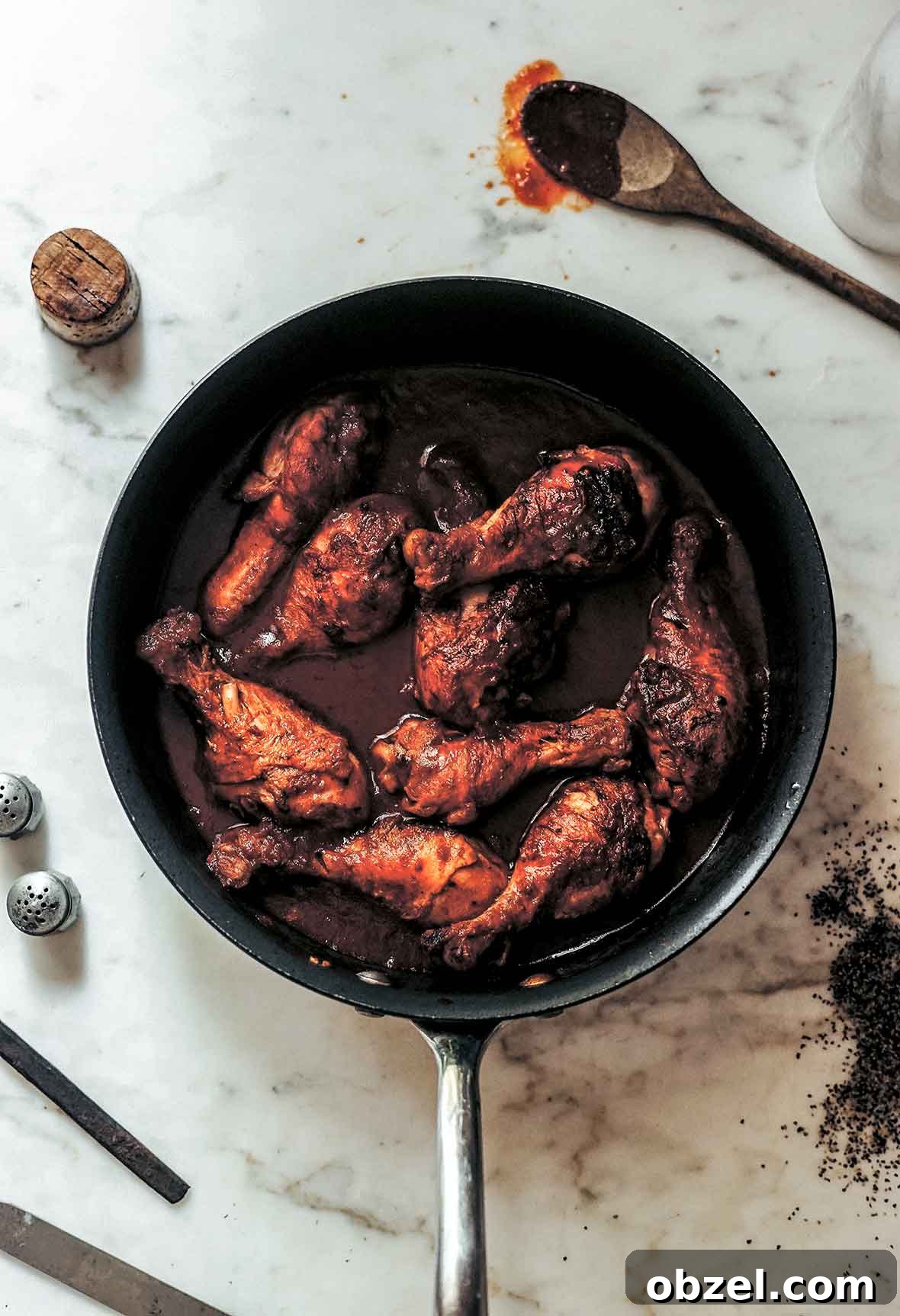 What Is Braising? Cooking Method, Tips, and Uses 5 A skillet filled with chicken drumsticks braised in wine with a wooden spoon and wine cork lying beside the skillet.