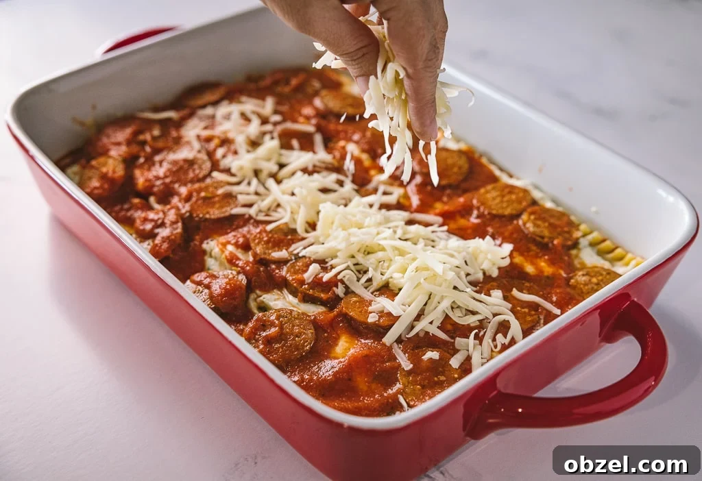 Smoked Italian Sausage Lasagna Recipe 4 Cheese being sprinkled on top of a rectangular baking dish of smoked Italian sausage lasagna.