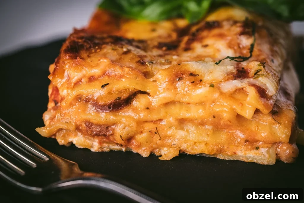 Smoked Italian Sausage Lasagna Recipe 6 A slice of smoked Italian sausage lasagna on a black plate with a metal fork in the foreground.