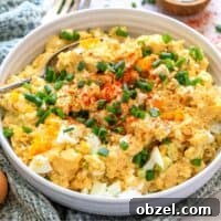 Deviled Egg Potato Salad Recipe 10 White ceramic bowl with deviled egg potato salad. Green onions on top and to the side with a spoon. Up close photo.