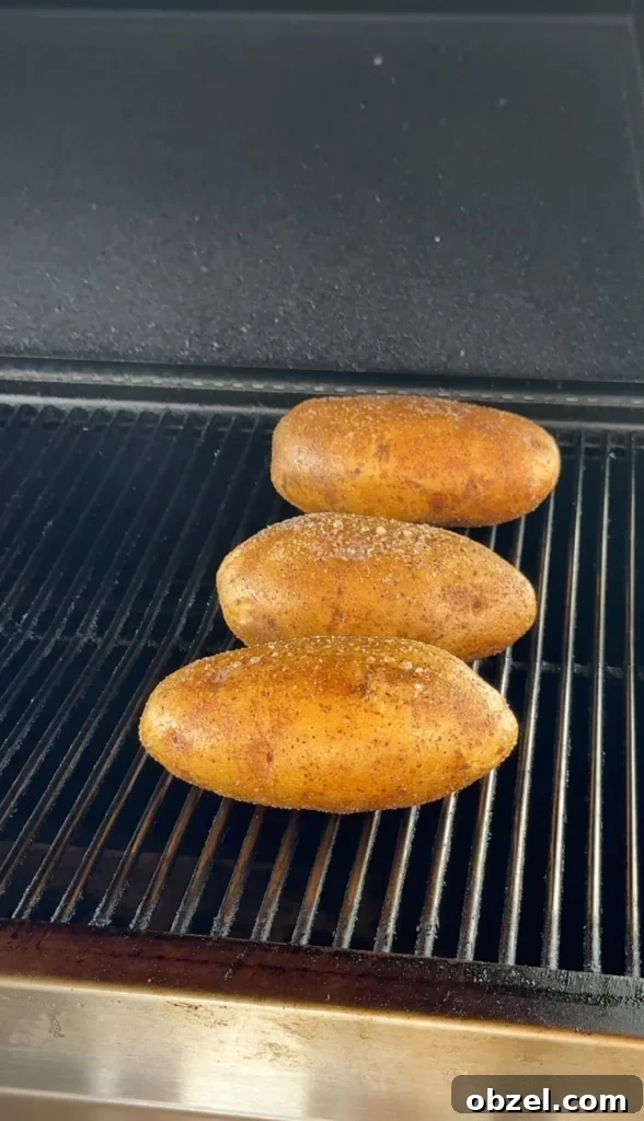 Loaded Baked Potatoes with Grilled Steak Bites 3 Russet potatoes wrapped in foil cooking on grill grates over indirect heat for perfect steakhouse-style baked potatoes