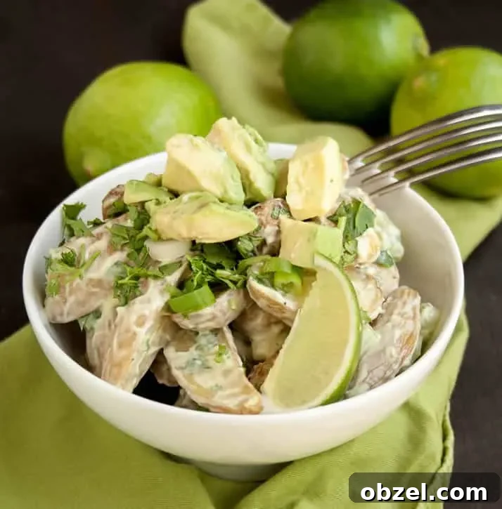 A bowl of Roasted Potato Salad with Avocado Lime Dressing with fork and limes in the background from themerchantbaker.com