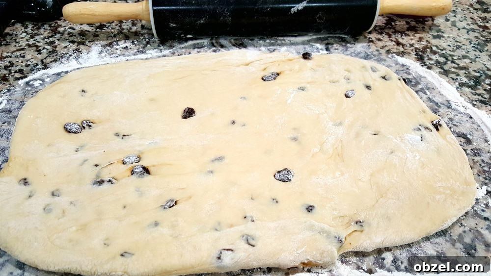 Cinnamon Raisin Swirl Bread Recipe 5 Raisin bread dough with raisins rolled out into a rectangle with a rolling pin.