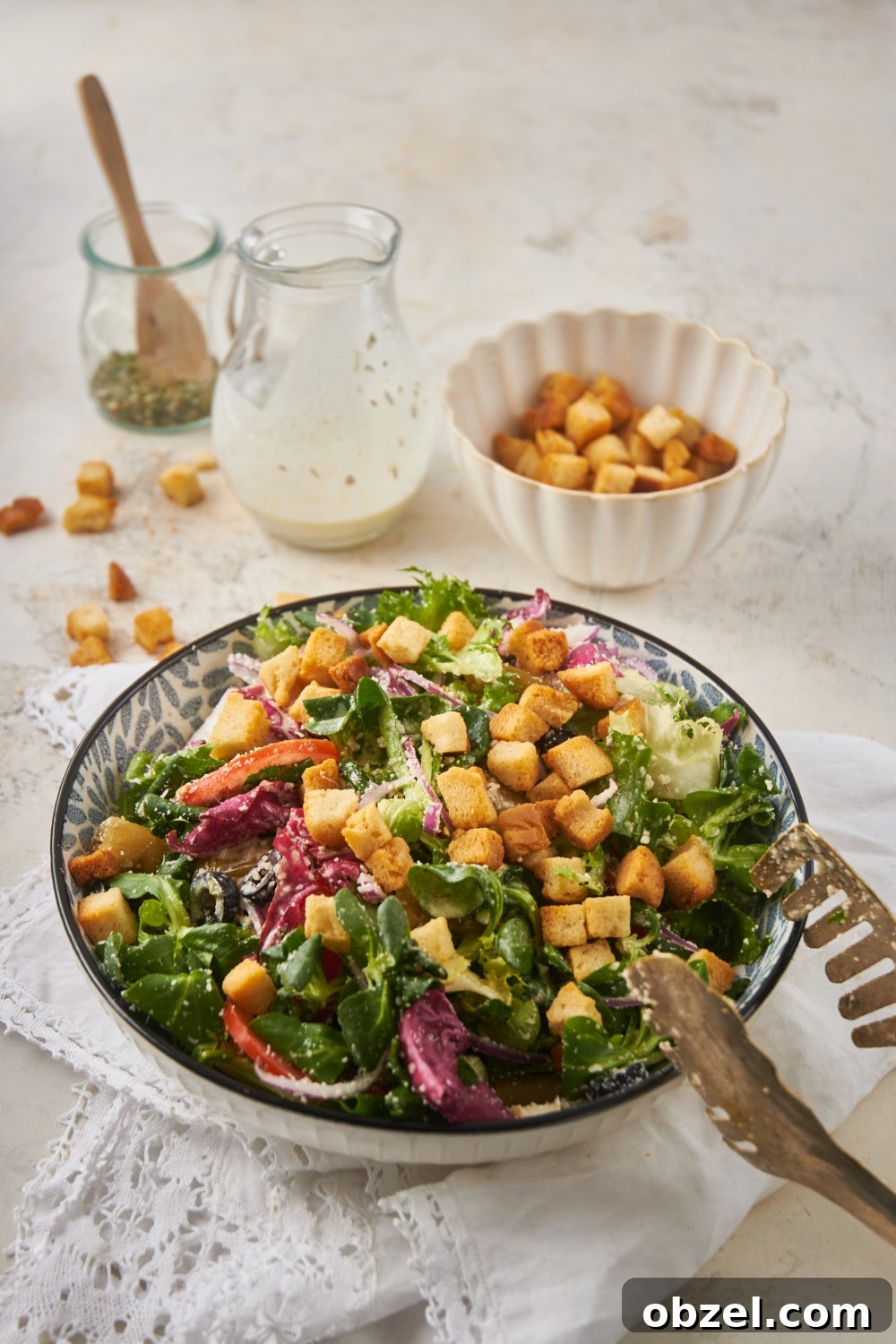 Olive Garden Salad Recipe with Homemade Dressing 3 A large bowl of salad filled with lettuce, peppers, onions, black olives, parmesan cheese, and croutons. A set of tongs is set on the side of the bowl.