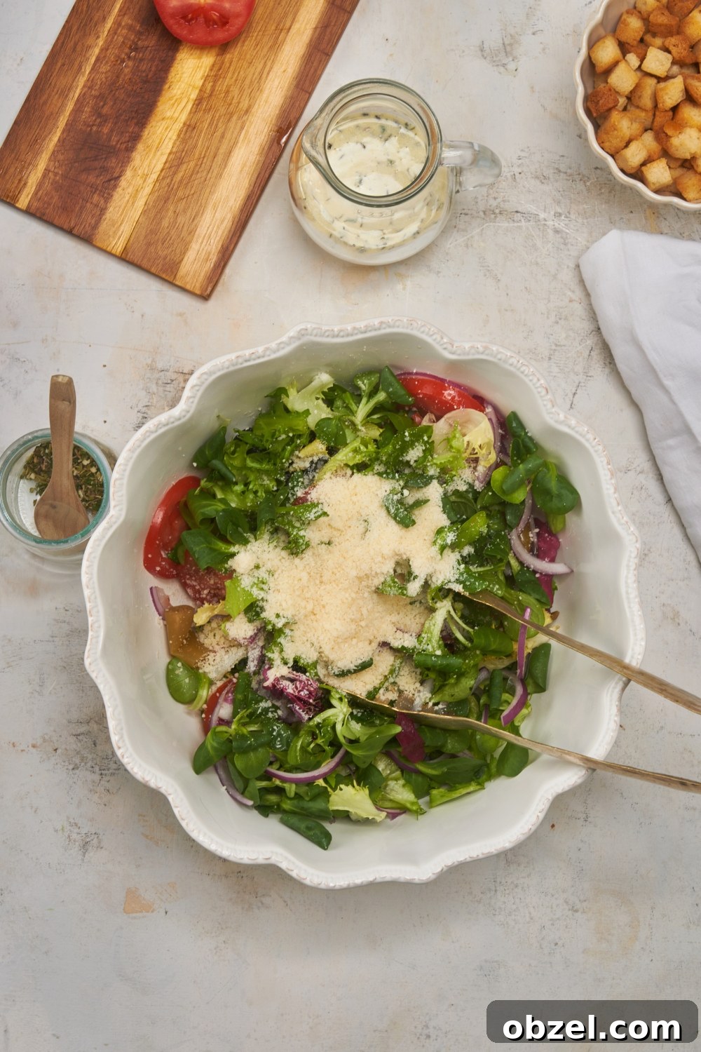 Olive Garden Salad Recipe with Homemade Dressing 6 A large white bowl filled with lettuce, tomatoes, onions, grated parmesan cheese and a set of tongs.