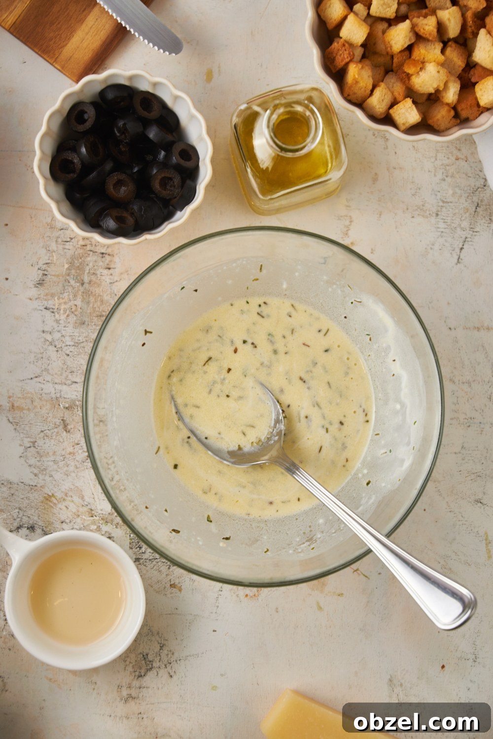 Olive Garden Salad Recipe with Homemade Dressing 7 A clear bowl filled with creamy Italian dressing and a spoon.