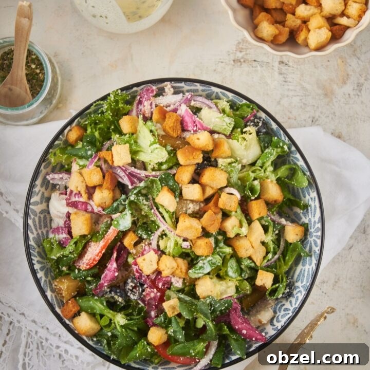 Overhead view of a salad filled with lettuce, peppers, onions, black olives, parmesan cheese, and croutons.