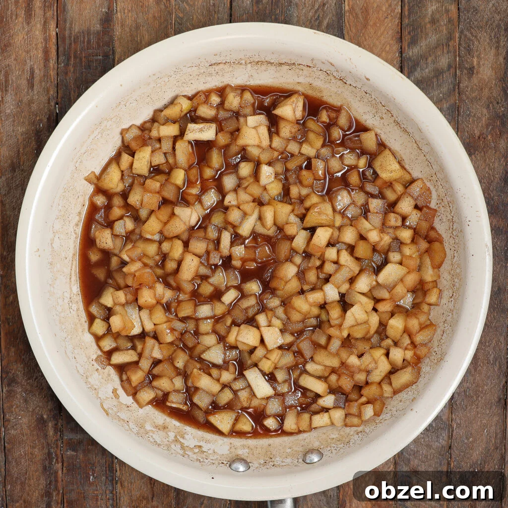 Caramel Apple Tiramisu Recipe: Autumn Dessert Twist 3 Diced apples simmer in a white skillet with a brown cinnamon sauce, evoking the warm flavors of caramel apple tiramisu on a rustic wooden surface.