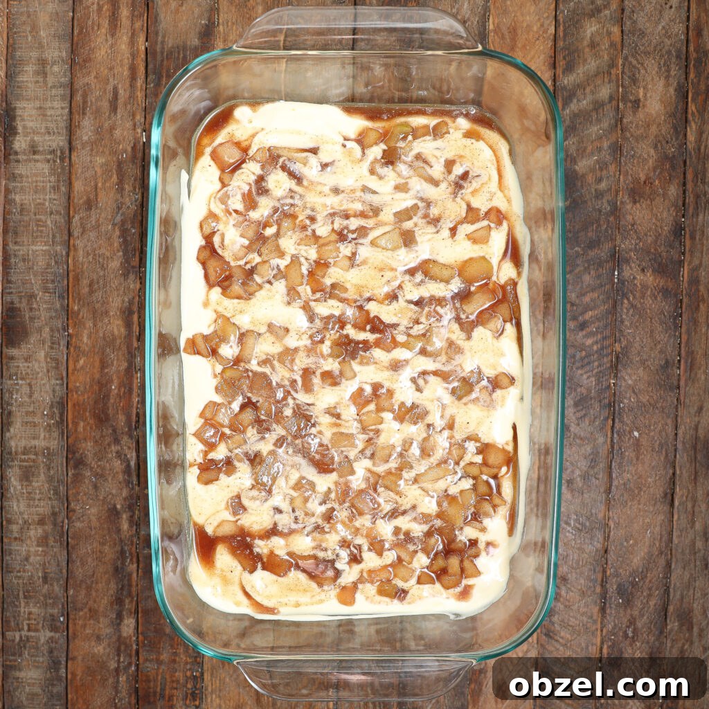 Caramel Apple Tiramisu Recipe: Autumn Dessert Twist 4 A glass baking dish filled with creamy caramel apple tiramisu, swirled with caramelized apple chunks, sits on a rustic wooden surface.