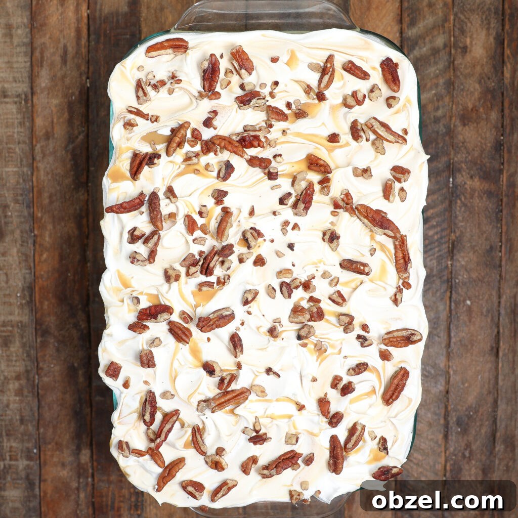 Caramel Apple Tiramisu Recipe: Autumn Dessert Twist 6 A rectangular baking dish filled with caramel apple tiramisu, topped with swirls of whipped topping, drizzles of caramel, and scattered pecans, placed on a rustic wooden surface.